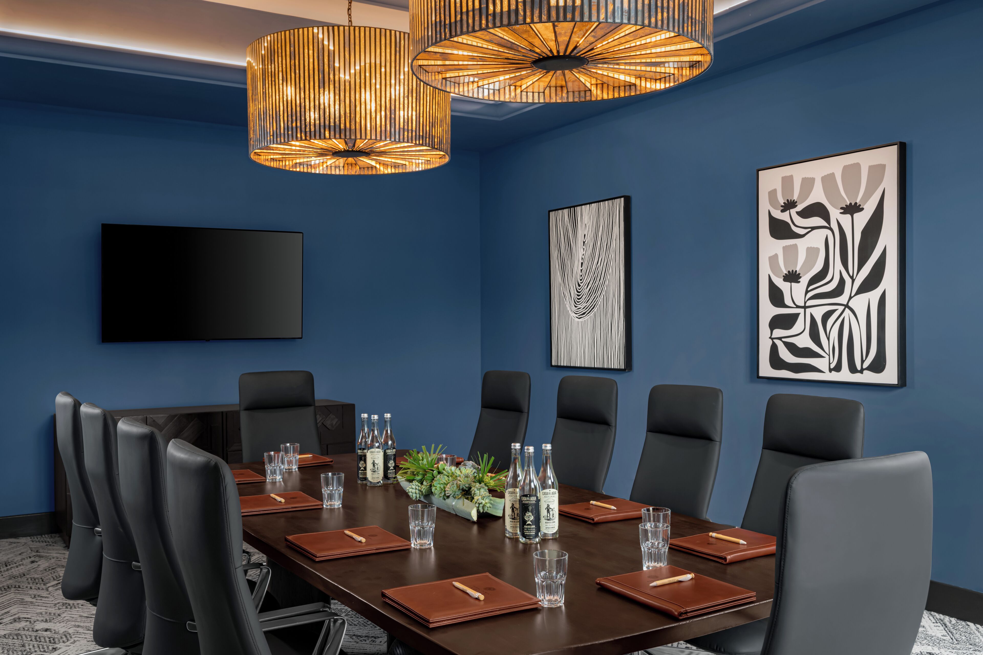 Un salón de conferencias con una mesa de madera oscura, sillas de cuero negro y una pantalla grande en la pared.