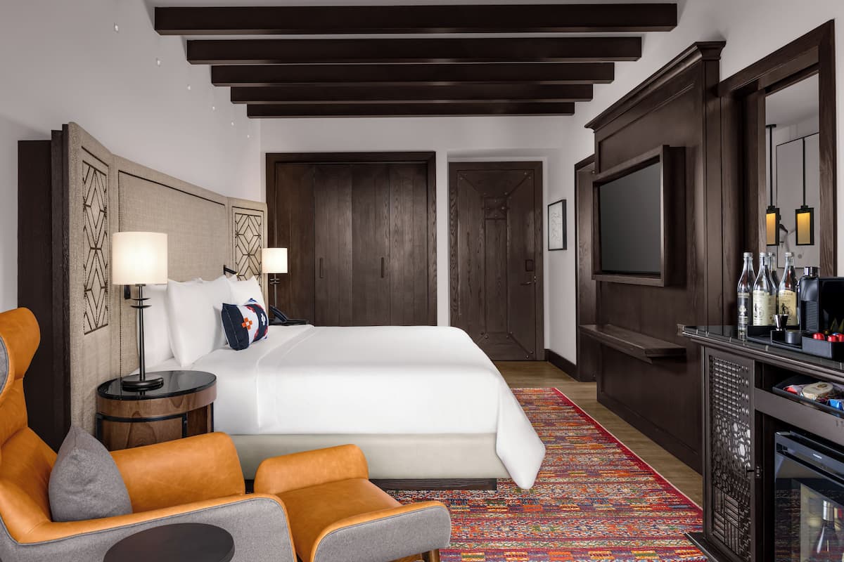 Ein Hotelzimmer mit einem großen Bett, einer Sitzecke mit zwei Sesseln, einem Fernseher, einer Minibar und einem gemusterten Teppich.