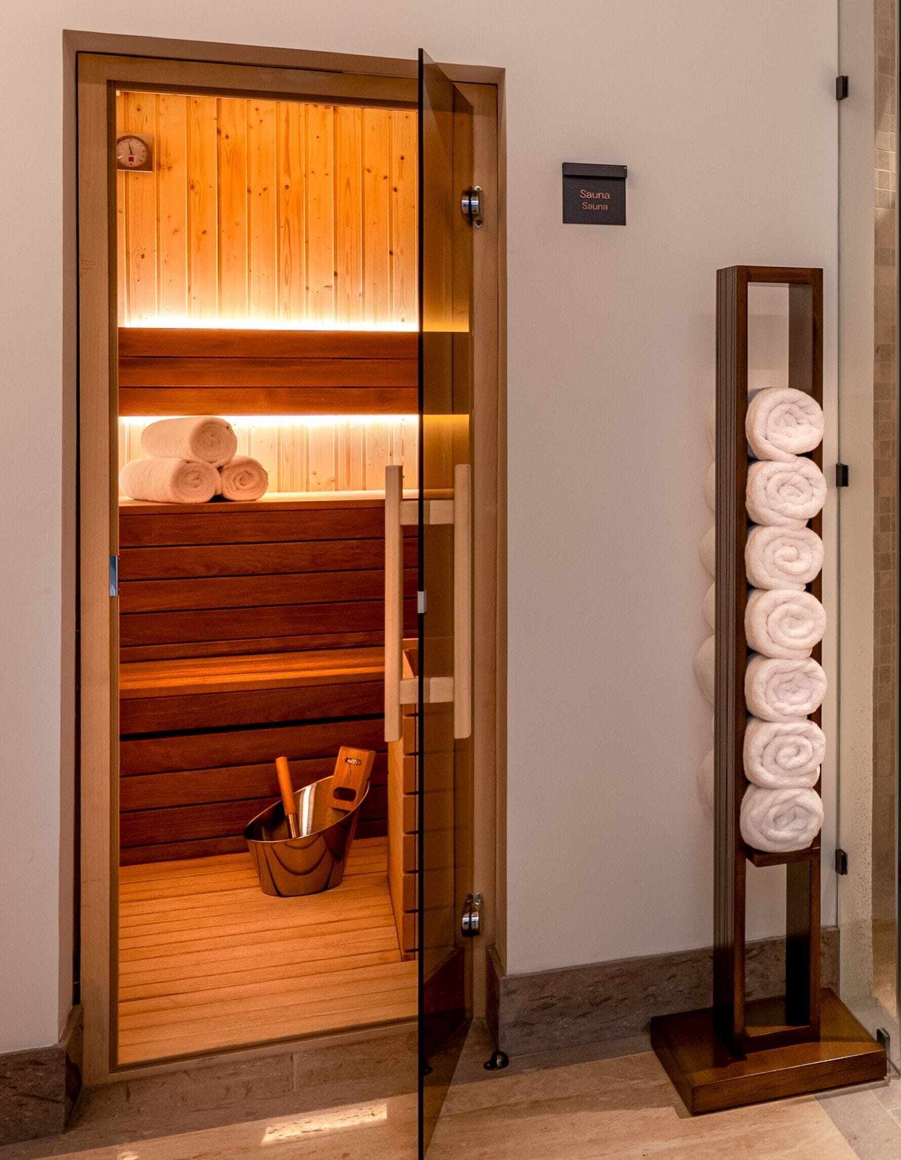Een sauna met houten banken, een handdoekrek en een emmer met handdoeken.