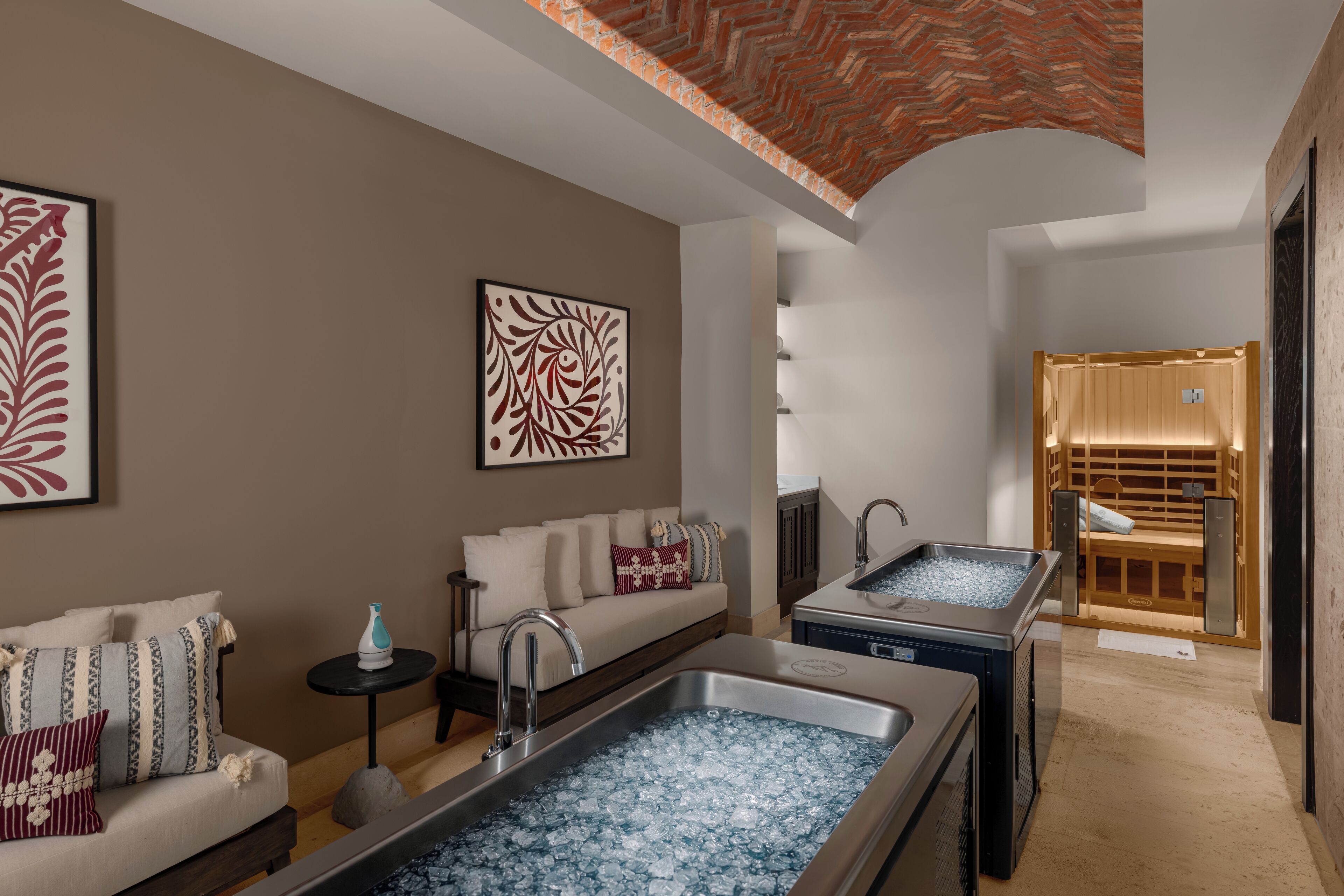 A modern spa room with a sofa, two large tubs, and a wooden sauna.