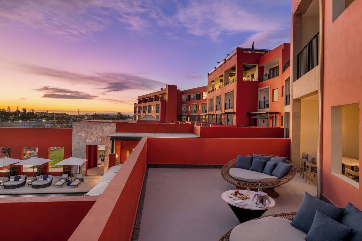 Eine Dachterrasse mit Sitzgelegenheiten im Freien, einer Steinmauer und Blick auf die Stadt bei Sonnenuntergang.