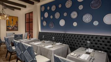 Uma sala de jantar com mesas postas para quatro, uma grande parede com pratos decorativos e uma cabeceira estofada.