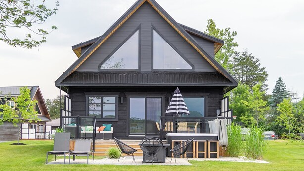 Une maison moderne, dotée d’une façade sombre, de grandes fenêtres et d’une terrasse aménagée avec du mobilier d’extérieur.