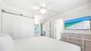 A bedroom with a large bed, a ceiling fan, a TV on the wall, and a dresser. - One Bed/ One Bath Condo- Step From Siesta Key Beach with Pool On Property! (Siesta Key)