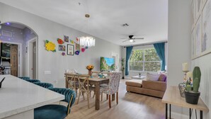 Una sala de estar moderna con comedor, piso de madera, ventilador de techo y un ventanal con cortinas.