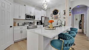 Una cocina moderna con armarios blancos, una isla central y taburetes de color turquesa.