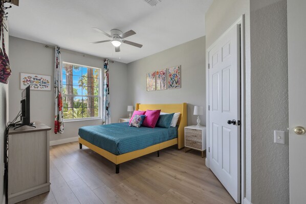 A bedroom with a bed, a ceiling fan, a window with curtains, a desk, and a door. - Poolside/waterpark in backyard. 1st floor Encanto theme w/Arcade next to Disney! (Kissimmee)