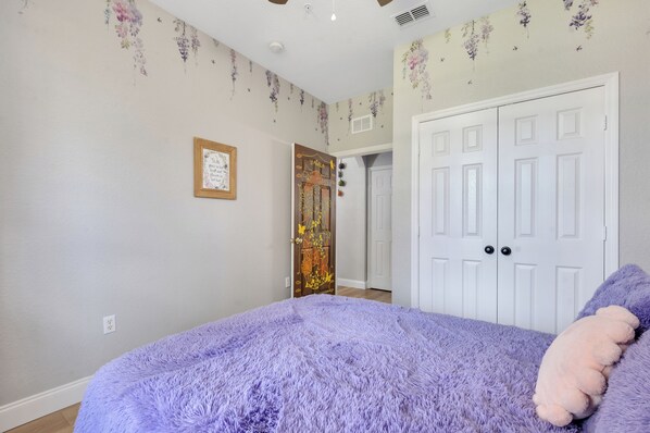 A bedroom with a purple fluffy bedspread, a white door, and floral wallpaper. - Poolside/waterpark in backyard. 1st floor Encanto theme w/Arcade next to Disney! (Kissimmee)