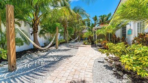 A paved pathway lined with palm trees and a hammock, leading to a building with a sign. - Beautiful Two Bedroom/ Two Bath Bianco Sands, Quick Walk to Beach! (Siesta Key)