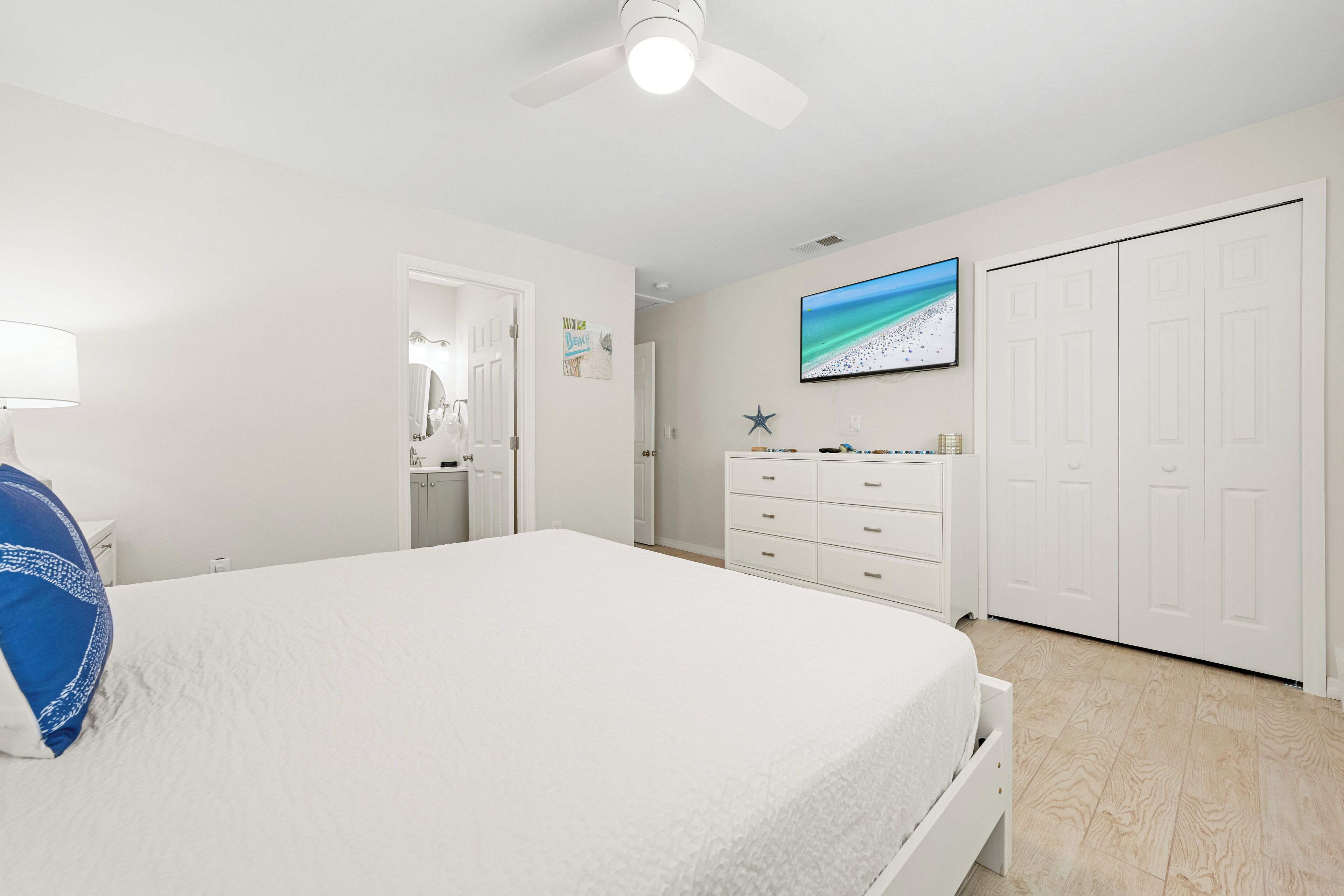 Une chambre à coucher comprenant un lit, une commode, un placard, un ventilateur de plafond et un téléviseur fixé au mur.
