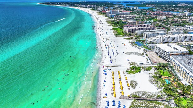 An aerial view of a coastal city with a wide beach, clear turquoise waters, and a mix of residential and hotel buildings. - Beautiful Two Bedroom/ Two Bath Bianco Sands, Quick Walk to Beach! (Siesta Key)