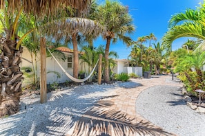 A pathway leading to a building with a thatched roof, surrounded by palm trees and a gravel path. - Beautiful Two Bedroom/ Two Bath Bianco Sands, Quick Walk to Beach! (Siesta Key)