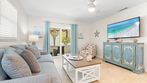 A living room with a sofa, coffee table, and a television on a wall. - Beautiful Two Bedroom/ Two Bath Bianco Sands, Quick Walk to Beach! (Siesta Key)