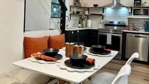 Una cocina moderna con comedor, que incluye una mesa blanca, platos negros y rojos, y una campana extractora de acero inoxidable.