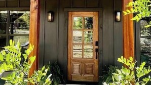 Un edificio con puerta de madera, un porche con plantas y techo de metal.