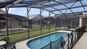 Una piscina exterior cubierta con zona vallada, rodeada de casas y un césped.