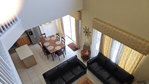 Amplia sala de estar con una mesa de comedor y sofás de cuero negro, una mesa de centro de madera y una cocina al fondo.