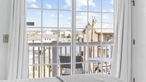Una habitación con un ventanal grande, cortinas blancas y vista a una zona residencial con casas y un muelle.