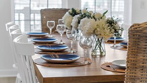 Una mesa de comedor dispuesta con platos azules, sillas blancas y flores blancas.