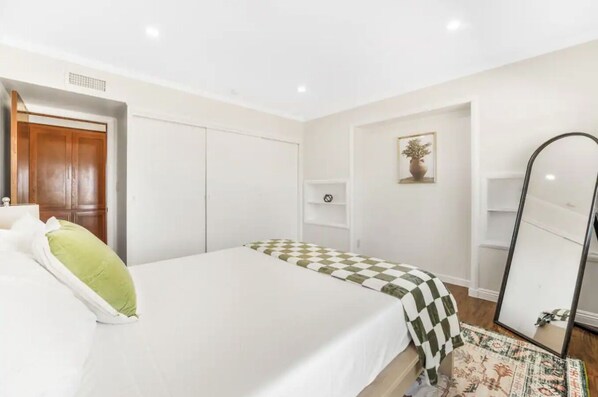 A bedroom with a bed, a wardrobe, a mirror, and a shelf.