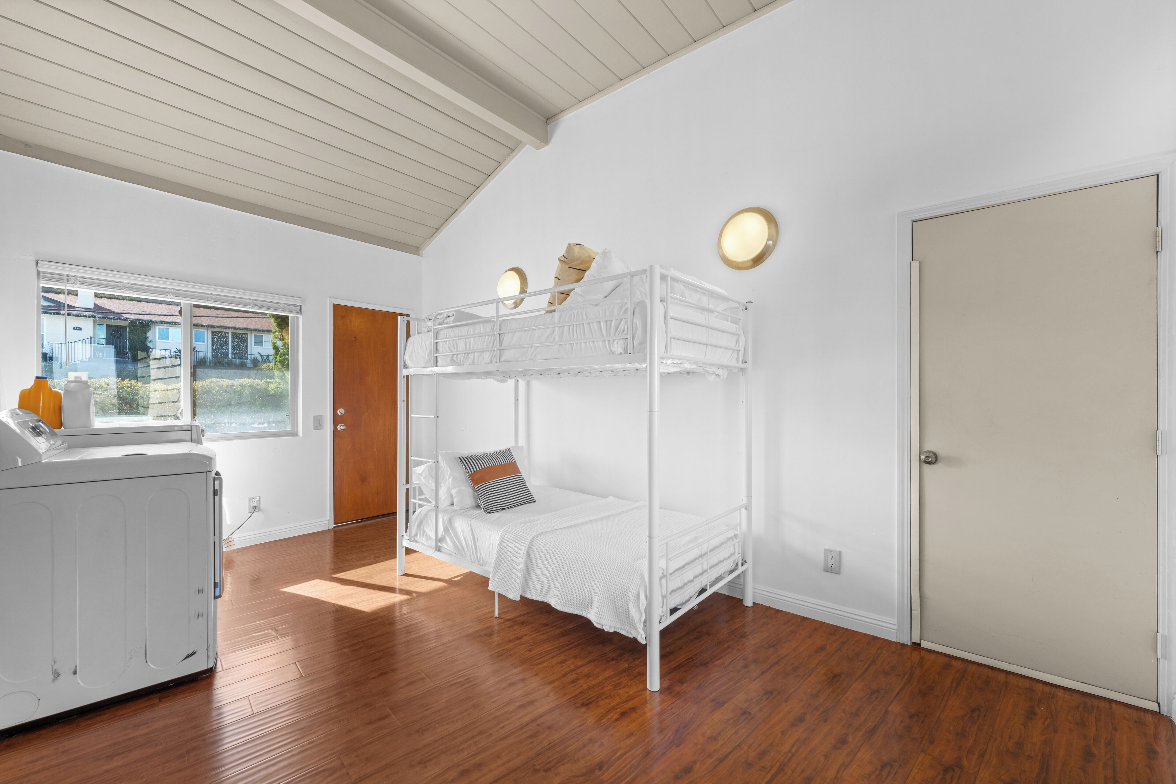 Ein Zimmer mit einem Etagenbett, einer Waschmaschine, einem Fenster mit Blick und einer Tür.