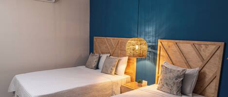 A hotel room with two beds, a wooden headboard, a bedside lamp, and a wall-mounted air conditioner.