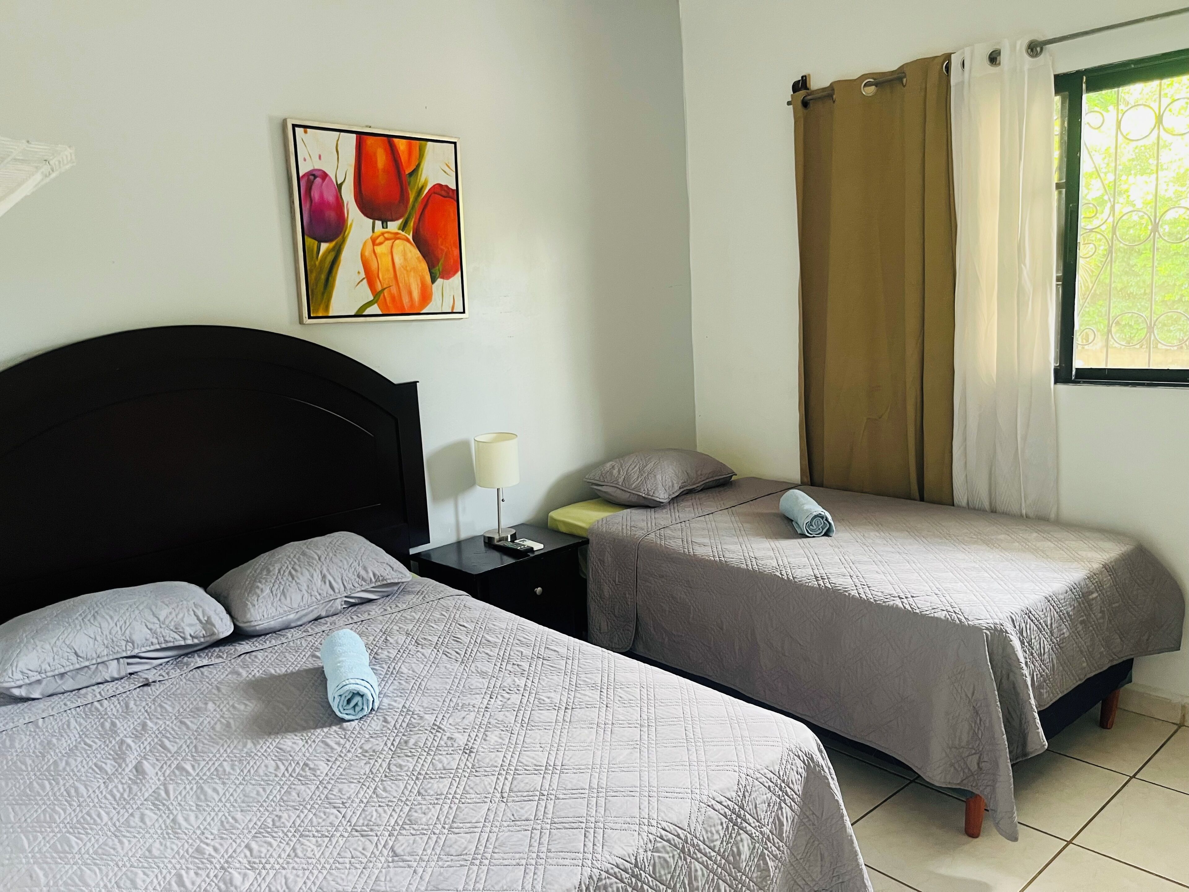 Une chambre d’hôtel avec deux lits, une table de chevet, une lampe et une fenêtre avec des rideaux.