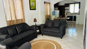A living room with a black sofa, a smaller black armchair, a woven rug, and a dining area with a table and chairs. - WE Hotel - La Lima (La Lima)