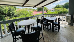 A covered outdoor seating area with tables and chairs, a white railing, and a view of greenery and buildings in the background. - WE Hotel - La Lima (La Lima)