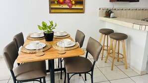 A dining area with a wooden table set for four, surrounded by chairs, and a kitchen area with a microwave and stools. - WE Hotel - La Lima (La Lima)