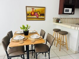A dining area with a wooden table set for four, surrounded by chairs, and a kitchen area with a microwave and stools.