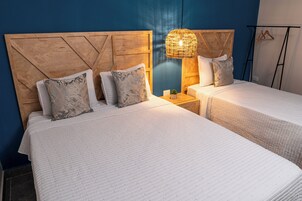 Habitación de hotel con dos camas, cabecera de madera, lámpara colgante y una planta pequeña en la mesita de noche.