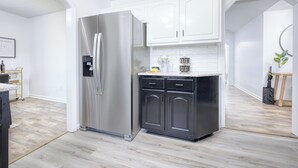 Una cocina moderna con armarios blancos, un refrigerador de acero inoxidable y piso de madera clara.