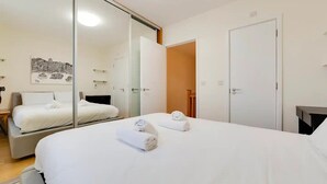 Habitación de hotel con una cama grande, una mesita de noche, un espejo y una puerta que da a otra habitación.