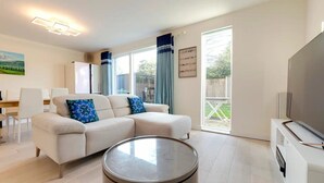 Una sala de estar moderna con un sofá, una mesa redonda de centro, un televisor y un comedor con sillas y una mesa.
