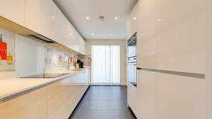 Una cocina moderna con armarios blancos, un lavamanos de acero inoxidable y una ventana con persianas.