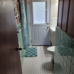 Un bagno con il water bianco, un lavandino, una doccia con porta in vetro e un tappeto a motivi sul pavimento.