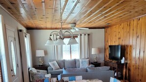 Ein großzügiges Wohnzimmer mit einer großen Couch, einem Esstisch mit Marmorplatte und einem Fernseher auf einem Holzständer.