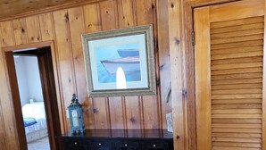 Ein Zimmer mit Holzpaneelen, einem dunklen Konsolentisch, einem gerahmten Bild und einer Tür mit Lamellen.