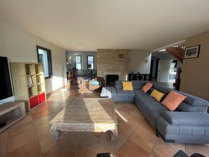 A spacious living room with a sectional sofa, a coffee table, and a stone fireplace. - Family house with covered & heated swimming pool, large private park near beach (Baden)