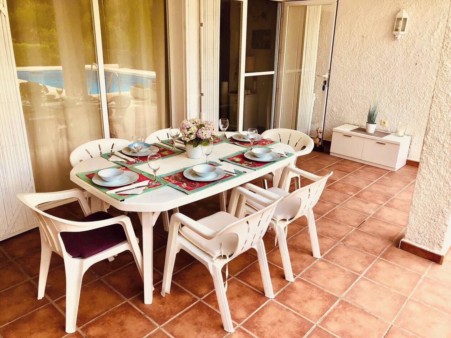 A dining area with a table set for four, white chairs, and a white cabinet with a plant and candle.