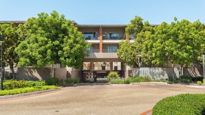 Un edificio de varios pisos con una entrada central, rodeado de jardines cuidados y un camino de entrada de grava.
