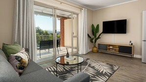 Una sala de estar moderna con un sofá, una mesa de centro de vidrio, un televisor y un ventanal corredero que da a un balcón.