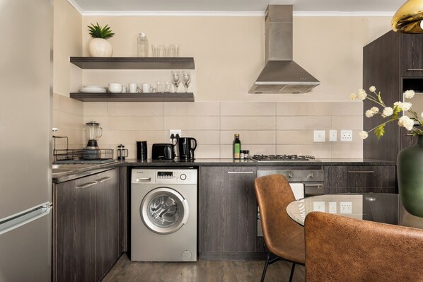 A modern kitchen with a built-in washer and dryer, dark wood cabinets, and a coffee station.