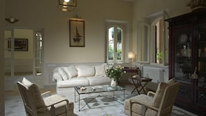 A spacious living room with a white sofa, two armchairs, a glass coffee table, and a decorative lamp.