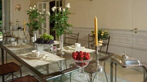 A dining table set with white tablecloths, clear glassware, and a variety of fruits and flowers.