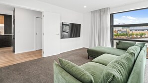 Una sala de estar moderna con un sofá verde, un televisor de pantalla plana y un ventanal con vistas al exterior.