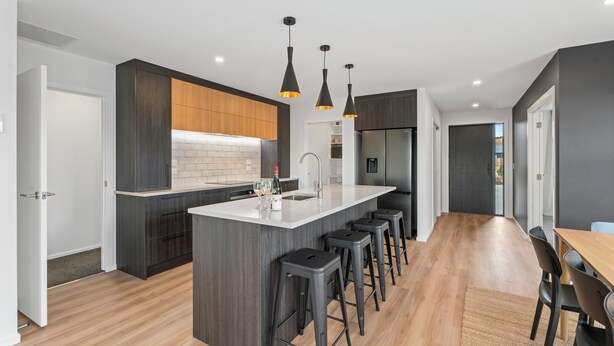 Una cocina moderna con una isla central, taburetes de bar, iluminación colgante y un área de comedor con mesa y sillas de madera.