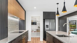 Una cocina moderna con armarios de madera oscura, encimeras blancas y un horno empotrado. Hay lámparas colgantes sobre el fregadero y un refrigerador a la derecha.