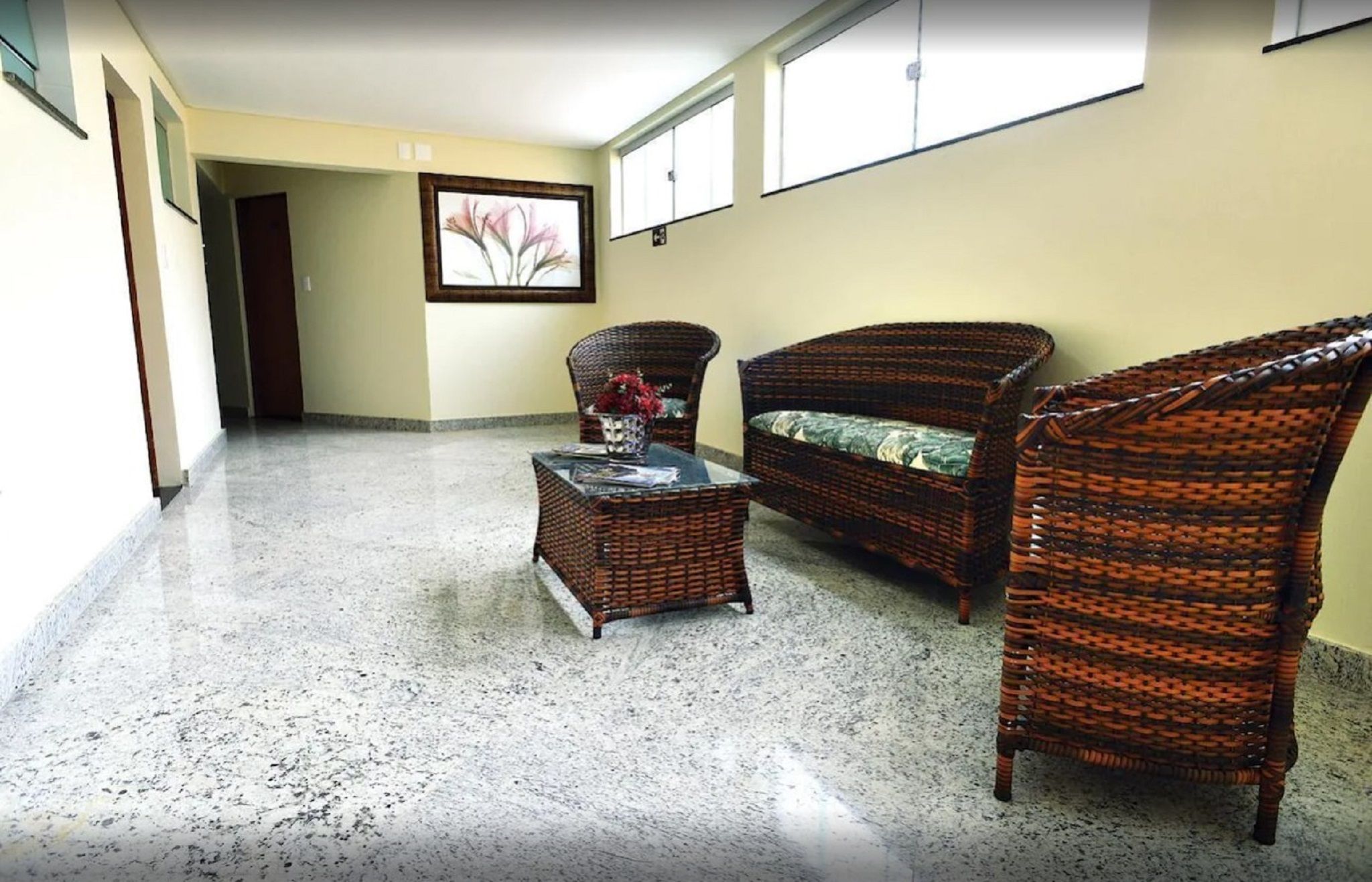 A hallway with wicker furniture, a glass coffee table, and a framed picture on the wall.